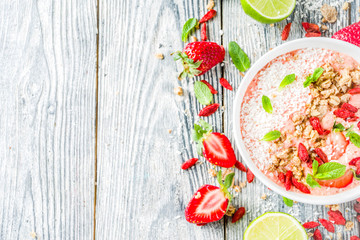 Healthy breakfast smoothie bowl with goji and strawberry berries, granola, yogurt, coconut, lime, wooden background copy space