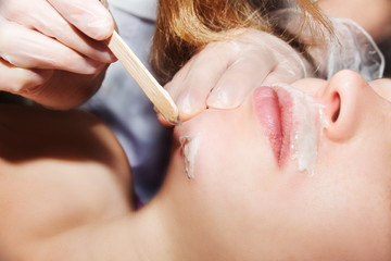 Depilation with hot wax mustache in the beauty salon. Young woman receiving facial epilation close up. Cosmetologist removes hair on face. Beauty salon, mustache depilation - obrazy, fototapety, plakaty