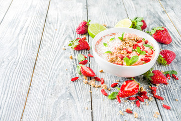 Healthy breakfast smoothie bowl with goji and strawberry berries, granola, yogurt, coconut, lime, wooden background copy space