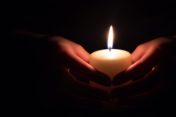 Female hand holding a burning candle in the dark
