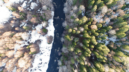 Aerial view of a river in the forest with snow along the banks.