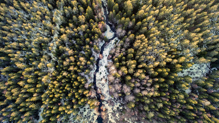 Aerial view of a river in the forest with snow along the banks.