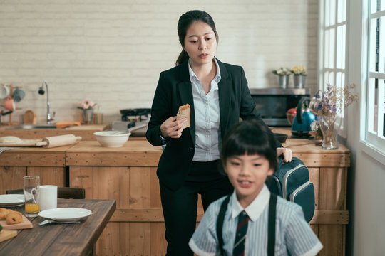 Young Busy Asian Employee Mother Rushing With Daughter In Morning Going Faster Late For Work And School. Mom Businesswoman Take Away Toast Breakfast Hold Backpack. Child In Uniform Smiling Walk Leave