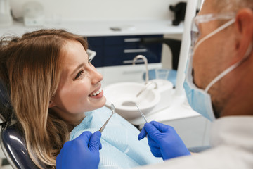 Image of caucasian woman sitting in dental chair while professional doctor fixing her teeth