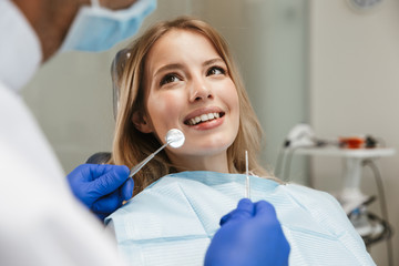 Image of smiling woman sitting in dental chair while professional doctor fixing her teeth