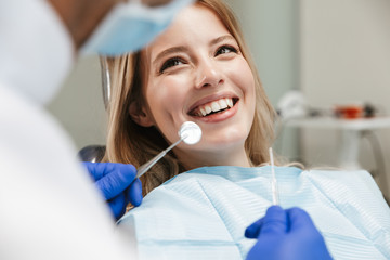 Image of pretty woman sitting in dental chair while professional doctor fixing her teeth