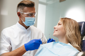 Image of lovely woman sitting in dental chair while professional doctor fixing her teeth