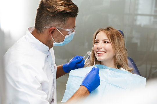 Image of blond woman sitting in dental chair while professional doctor fixing her teeth