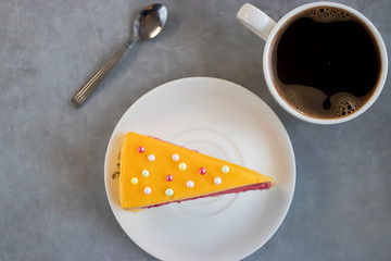 A piece of mousse cake with a taste of mango and strawberry on a white plate and a cup of coffee.
