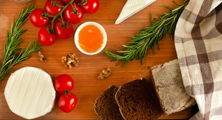Rye bread with brie and camembert cheeses, nuts, honey, cherry tomatoes and rosemary on a wooden board
