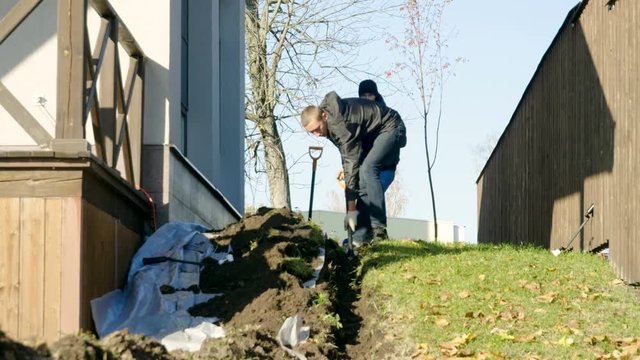 Two men digging a trench using shovels to make automatic watering of plants in the garden. 4K