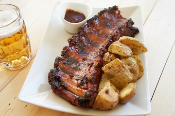 Grilled pork ribs with baked potatoes, barbecue sauce and beer pitcher.