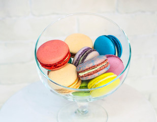 bright colored and marbled macaroons in glass vase on white brick background.