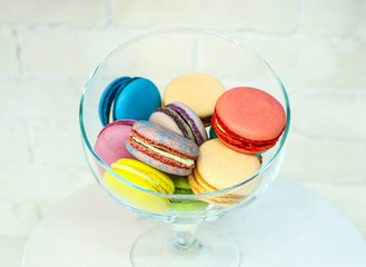 bright colored and marbled macaroons in glass vase on white brick background.