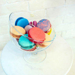 bright colored and marbled macaroons in glass vase on white brick background.