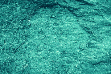 Vintage azure background. Rough painted wall of turquoise color. Imperfect plane of cyan colored. Uneven old decorative toned backdrop of aqzure tint. Texture of teal hue. Ornamental stony surface.