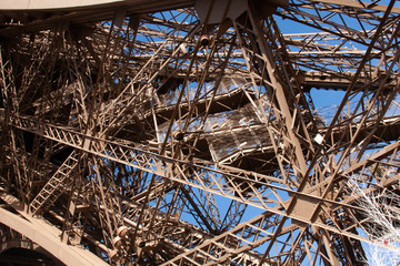 The underneath of the Eiffel tower showing the construction and steel girders against a blue sky