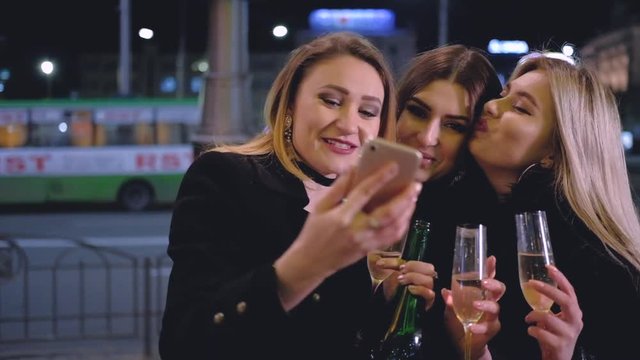 Girls night out celebration. Party mood. Ladies taking selfie, standing with champagne on the street with blur city lights.