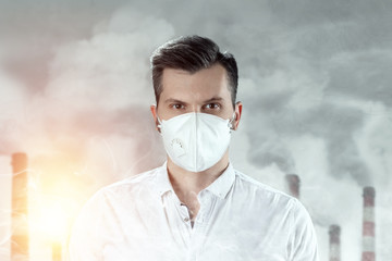 A man in a white mask because of air pollution in the city on the background of pipes. Protecting the body from global warming. Dust mask in the city. The concept of air pollution, carbon dioxide.