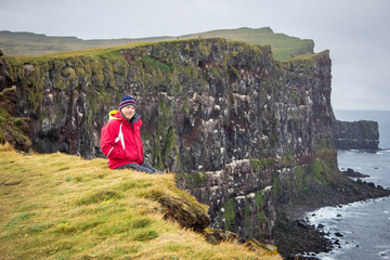 The man sitting on the edge of a cliff in western fjords of Iceland near Atlantic ocean shore, coastline. Latrabjarg, famous rookery. Happy man amid icelandic nature. Waterproof, outdoor activity.