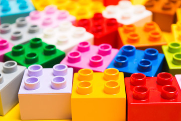 Many colorful plastic bricks of toy child constructor on yellow background