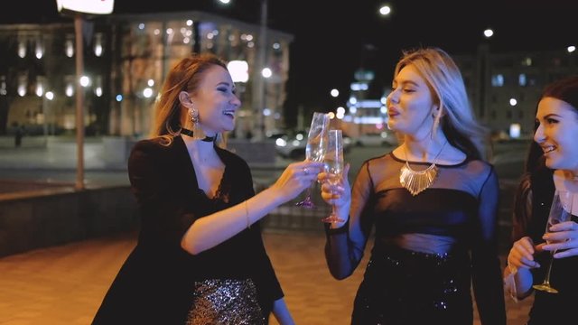 Girls night out party. Ladies in cocktail dresses walking down the street with champagne. Special event. Blur city lights.
