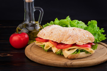 Ciabatta sandwich with lettuce , prosciutto and  cheese on wooden board