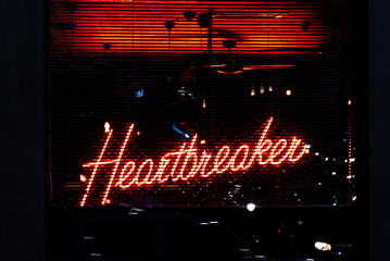 A red neon sign displaying the words 'Heartbreaker' is glowing behind window blinds