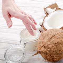 Coconut oil on human palm and in airtight glass jar with shell pieces aside on white wooden table