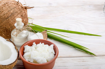 Background of coconut, coconut shell, oil in clay bowl and glass jar on white wooden table