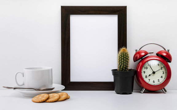 MockUp dark photo frame, a red alarm clock, a cactus, crackers and a white cup of coffee with a saucer on a light background. Scandinavian style