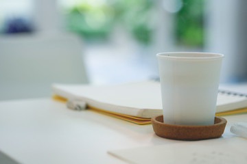 A paper cup of coffee on the table with note book.