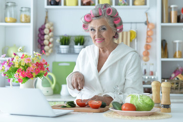 Portrait of senior woman in hair rollers cutting vegetables on kitchen table