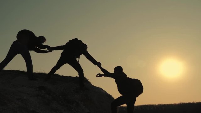 Silhouettes of tourists climbing mountain cliffs against the backdrop of a sunset, helping each other's hand. Help in the mountains and teamwork in hiking. Teamwork concept.