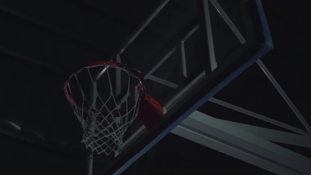 Close up image of professional basketball player making slam dunk during basketball game in floodlight basketball court.