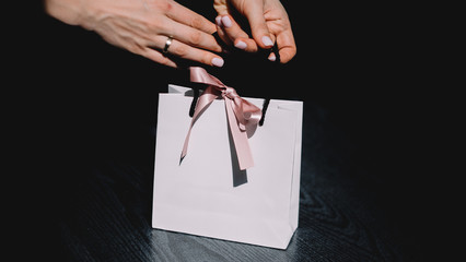 Woman holds paper bag on black background. Women with beautiful manicure. White paper beg with pink...