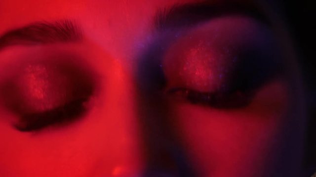 Closeup shoot of pretty female eyes with seductive vogue makeup with red neon light and bokeh background looking at camera at nightclub