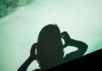 Abstract background shadow silhouette of female woman screaming scared holding head with hands on digital wall light from cinema projector on a wall