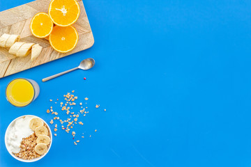 granola with banana slices and orange juice for breakfast on blue background top view copyspace
