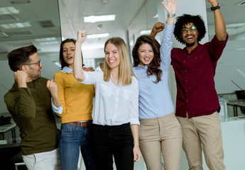 Obraz premium Group of young excited business people with hands up standing in office