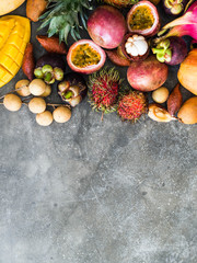 Various fresh Thai fruits - rambutan, mango, mangosteen, longan, papaya, dragon fruit, sapodilla, passion fruit, salak, pineapple on a wooden tray and a gray background. Top view. Copy space