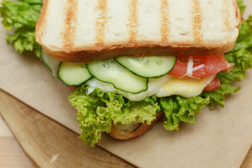 Closeup juicy sandwich with bacon, fresh vegetables, green salad and dark lines after grill