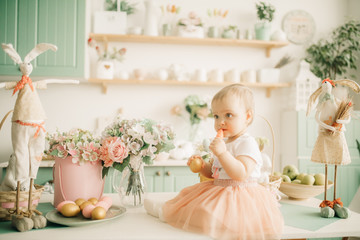 Toddler girl sits and eats a carrot among the easter decorations.