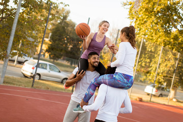 Obraz premium Young women sitting on the men shoulders and holding a basketball at outdoor court
