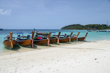 Long-tail wooden boats anchored on white beach in tropical sea