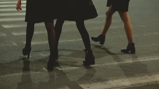 Girls out. Festive mood. Female friends walking with champagne at night, crossing road, having fun. Blur city lights background.
