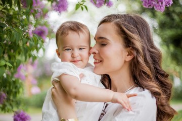 Beautiful young mother and little cute daughter are happy near the lilac. Portrait of mom and daughter. Spring.