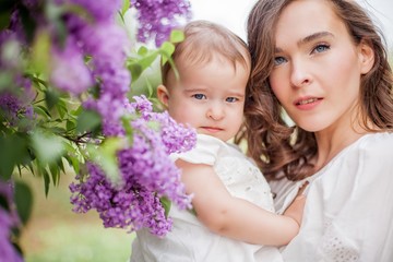 Beautiful young mother and little cute daughter are happy near the lilac. Portrait of mom and daughter. Spring.