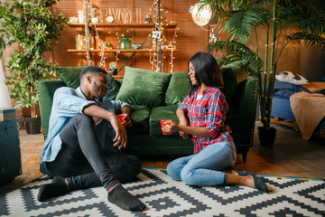 Black couple sitting on floor and drinks coffee