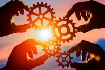 Four gears in the hands of people against the sky. teamwork. the mechanism of interaction.